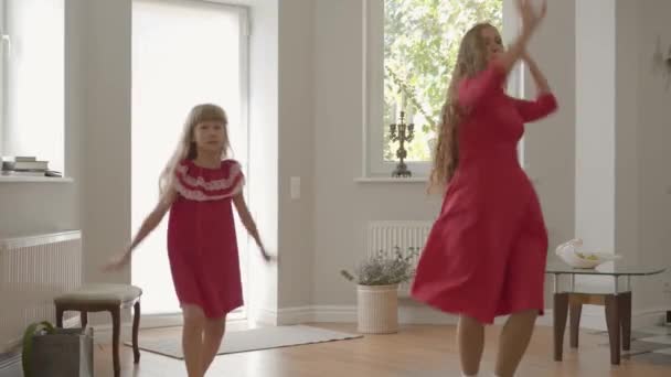 金发碧眼的母亲和女儿在周末玩得很开心。美丽的女人和开朗的女孩在相同的红色礼服跳舞。快乐的家庭一起度过一天. — 图库视频影像