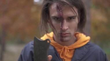 Yakışıklı adam yüzüne büyük çirkin yara gösteren kameraya yüzünü çevirerek sonra onun cleaver gösterir. Yüzünde Cadılar Bayramı makyajı olan adam kötü bir gülümseme ile bıçağını ovuşturarak