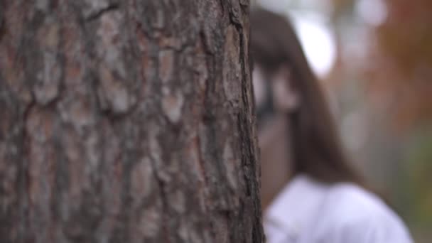 Ritratto di una bella donna con lo sguardo fuori da dietro un albero con il trucco del cranio sul viso mostra grande mannaia e si nasconde di nuovo. Celebrazione di Halloween. Telecamera in movimento destra e sinistra — Video Stock