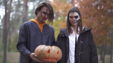 Uzun boylu yakışıklı adam içinde bir ışık ile halloween balkabağı tutan, güzel kız yanında duran, her ikisi de gülümseyerek sonra kötü yüzler yapma. Ormanda kameraya bakan yüzlerinde korkunç makyaj olan insanlar