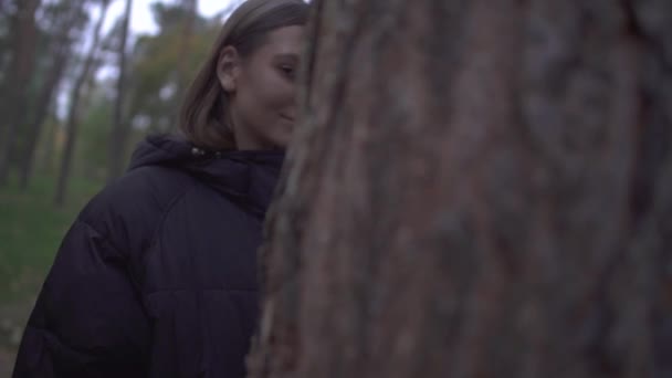 Jolie fille en manteau chaud regardant par derrière un arbre souriant. La caméra se déplace vers un autre côté du coffre et il y a le visage de la même femme avec le maquillage du crâne dessus. Fête d'Halloween 