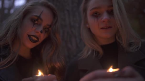 Dos chicas rubias jóvenes con aterrador maquillaje de halloween sosteniendo pequeñas velas en las manos y mirando a la cámara. Noche de terror gótico. Mujeres caucásicas listas para la noche de todos los santos . — Vídeos de Stock