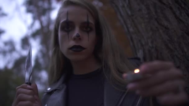 Mooie blonde psycho meisje met gruwelijke Halloween Make-up houder Hatchet en kleine kaars in handen. Jonge blanke vrouw lachend en op zoek naar de camera. Gothic alle heiligen nacht — Stockvideo