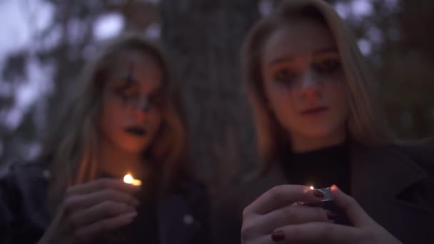 Retrato de dos niñas con el maquillaje de Halloween en las caras con velas pequeñas en las manos mirando en la cámara. Noche de terror de gente gótica. Cambio de enfoque. Cámara acercándose cada vez más — Vídeo de stock