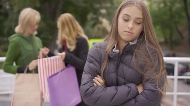 Fiatal szomorú nő érzés irigység az előtérben, míg ő két gyönyörű szőke barátnője állt az utcán mutatja egymásnak bevásárló táskák — Stock videók