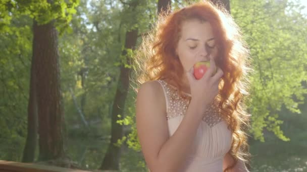 Belle femme caucasienne en vêtements blancs mangeant de la pomme rouge dans le parc d'automne. Vue rapprochée . — Video