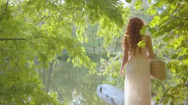 Young caucasian woman in light dress walking through the forest to the bank of the lake. Fairy-looking girl in white clothes resting in the autumn park. — Stockvideo