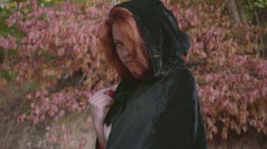 Siyah elbiseli gizemli kızıl saçlı beyaz kız kameraya dönüp kırmızı elmayı öneriyor. Sonbahar ormanında peri masalı perisi veya dryad. Pamuk Prenses stili.