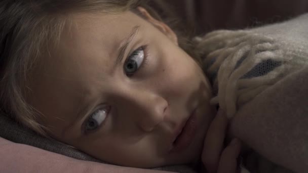 Cara de cerca de niña caucásica enferma tosiendo mientras está acostada debajo de una manta en casa. El niño triste tiene fiebre. Concepto de salud, enfermedad, enfermedad, resfriado común, tratamiento — Vídeo de stock