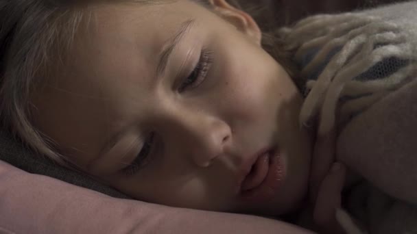 Cara de cerca de niña caucásica enferma tosiendo mientras está acostada debajo de una manta en casa. El niño triste tiene fiebre. Concepto de salud, enfermedad, enfermedad, resfriado común, tratamiento — Vídeo de stock