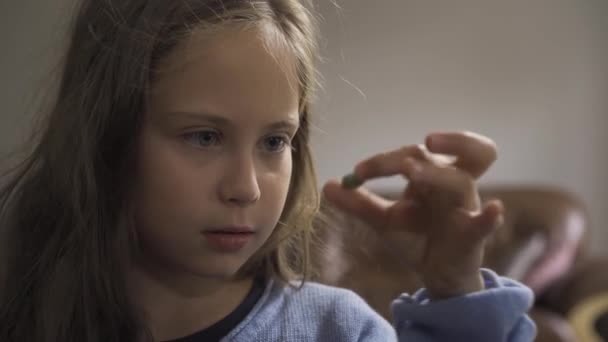 Close-up rosto de menina caucasiana doente engolindo uma pílula de ervas verdes e sorrindo enquanto sentado em casa. A criança tem febre. Conceito de saúde, doença, doença, resfriado comum, tratamento — Vídeo de Stock