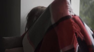 Hasta beyaz çocuk evde pencere üzerinde oturan sıcak bir battaniye ile kaplı. Ne yazık ki pencereye bakan ateşi olan küçük esmer kız. Sağlık kavramı, hastalık, hastalık, soğuk algınlığı, tedavi.