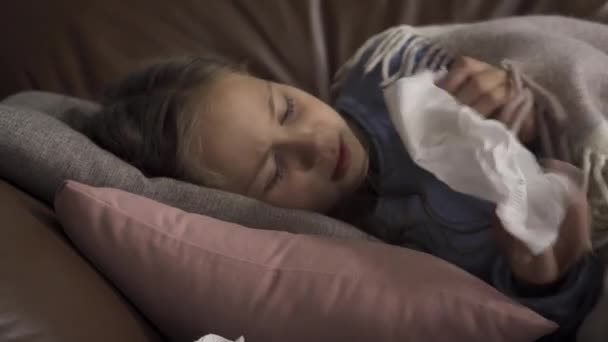Close-up van zieke jonge Kaukasische meisje hoesten en blazen neus terwijl liggend onder deken thuis. Het kind heeft koorts. Concept van gezondheid, ziekte, ziekte, verkoudheid, behandeling — Stockvideo