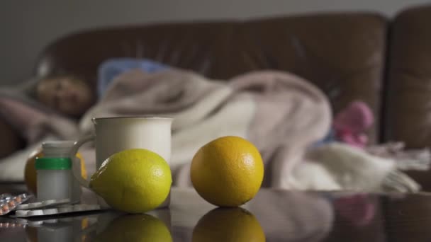 药片，柠檬和一杯茶的特写镜头与咳嗽的小白种女孩躺在背景。在家治疗儿童。焦点从背景到正面的变化. — 图库视频影像