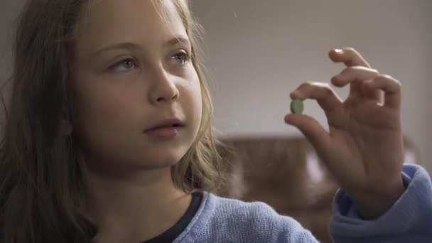 Close-up of sick little girl in blue sweater examining the green pill. Caucasian child undergoing treatment at home. — Stock Video