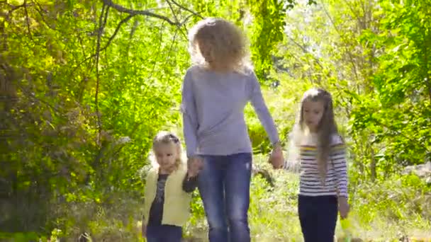 Ευτυχισμένη οικογένεια Καυκάσιων περπατά ανάμεσα στα δέντρα στο φθινοπωρινό πάρκο. Χαμογελαστή ενήλικη, σγουρή γυναίκα που κρατάει τα χέρια των μικρών όμορφων κορών της. Γυναίκες σε casual ρούχα ξεκουράζονται σε εξωτερικούς χώρους. — Αρχείο Βίντεο