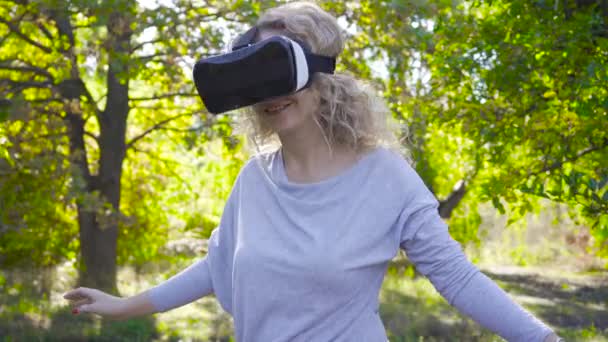 Портрет молодой женщины в очках VR, остановившейся в осеннем парке и улыбающейся. Красивая девушка в голубой блузке пробует виртуальную реальность на открытом воздухе . — стоковое видео