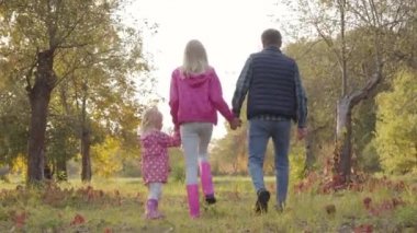 Sonbahar parkında pembe elbiseli iki kızıyla dolaşan beyaz bir adamın arka görüntüsü. Mutlu aile hafta sonları dışarıda birlikte vakit geçirir..