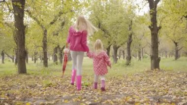 Pembe ceketli ve sonbahar ormanında yürüyen pembe lastik çizmeli iki sarışın kız. Kafkasyalı kız kardeşler hafta sonları dışarı çıkıyorlar..