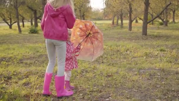 Kleines nettes blondes Mädchen, das der älteren Frau einen Regenschirm mit aufgemalten gelben Blättern schenkt. Zwei kaukasische Mädchen spazieren am Wochenende durch den Herbstwald. — Stockvideo