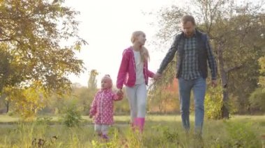 Güz parkında pembe elbiseli iki kızıyla dolaşan yakışıklı beyaz bir adam. Mutlu aile hafta sonları dışarıda birlikte vakit geçirir..