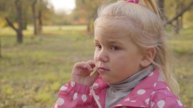 Sonbahar ormanında duran sevimli sarışın, beyaz bir bebeğin yakın plan portresi. Pembe elbiseli düşünceli çocuk ablasıyla dışarıda vakit geçiriyor..