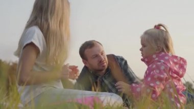 Mutlu beyaz bir ailenin sonbahar otlaklarında piknik yaptığı yakın plan. Güzel sarışın kızlar günlük giysiler içinde babaları birlikte oturup elma yiyorlar..