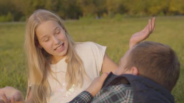 父親と感情的に話している若いブロンドの女の子のクローズアップ。秋の日を一緒に牧草地に座って過ごす家族. — ストック動画