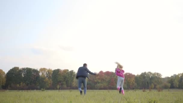 Кавказский отец и дочь бегут по осеннему лугу с розовым игрушечным самолетом, имитирующим муху. Счастливая семья отдыхает на открытом воздухе вечером перед закатом . — стоковое видео