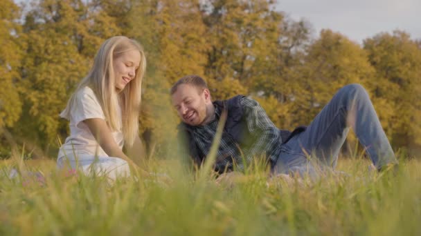 Baba ve kızı sonbahar çayırında oturup sohbet ediyorlar. Kafkasyalı bir adam ve genç sarışın bir kız günlük kıyafetler giyip birlikte dışarıda vakit geçiriyorlar.. — Stok video