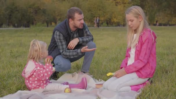 Bärtiger Kaukasier, der seine ältere Tochter auf der Herbstwiese anbrüllt. Blonder Teenager verteidigt sich und beschuldigt jüngere Schwester in pinkfarbener Jacke. — Stockvideo