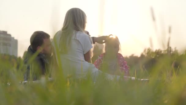 Família caucasiana feliz sentada no prado em raios de sol e comendo maçãs. Pai passar tempo com sua filha adolescente e pequena menina loira ao ar livre . — Vídeo de Stock