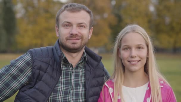 Retrato de cerca del padre caucásico y su hija rubia de pie en el parque de otoño. Familia feliz mirando a la cámara y sonriendo . — Vídeos de Stock