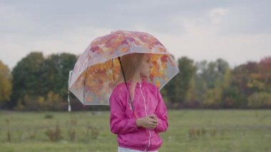 Pembe ceketli, sarı yapraklı, renkli şemsiyeli, üzgün, beyaz, sarışın kız. Güzel kız sonbahar çayırlarında vakit geçiriyor..