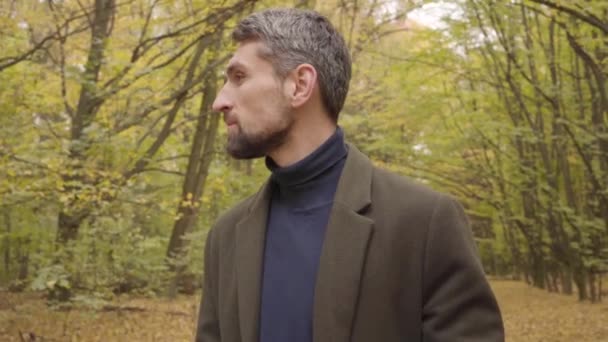 Primo piano di un uomo caucasico sicuro di sé con i capelli grigi e gli occhi marroni che si girano verso la fotocamera e sorridono. Bel ragazzo in abiti casual trascorrere i fine settimana nella foresta autunnale . — Video Stock