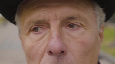 Kameraya bakan fındık rengi gözlü ve gri saçlı beyaz bir adamın aşırı yakın çekimi. Olgun adam düşünceli bir şekilde başını sallıyor..