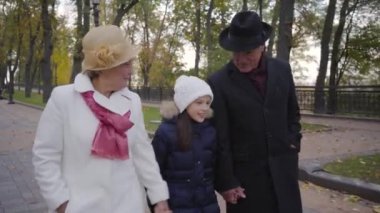 Beyaz şapkalı bir kızla sokakta yürüyen son sınıf beyaz tenli bir çiftin yakın çekimi. Büyükbabalar hafta sonlarını torunlarıyla sonbahar parkında geçirirler..