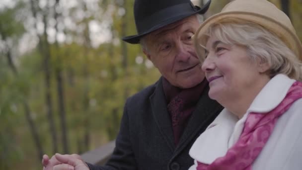 Close-up of a mature Caucasian couple standing next to the handrails and talking. Senior man and woman dressed in elegant classic clothes spending autumn day in the park. — ストック動画