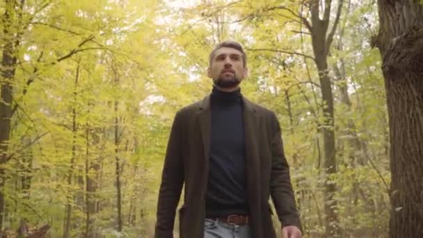 Close-up de um belo homem caucasiano confiante em roupas casuais andando na floresta. Cara com cabelos grisalhos e olhos castanhos desfrutando calmo dia de outono sozinho . — Vídeo de Stock