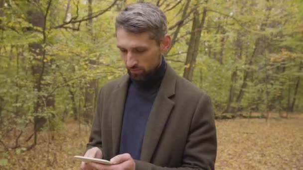 Hombre caucásico de confianza de pie en el bosque de otoño y usando su tableta. Turista guapo comprobando el camino en línea . — Vídeos de Stock