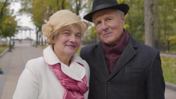 Usmívající se dospělý bělošský pár v elegantním oblečení, dívající se do kamery a usmívající se. Starší manžel a manželka si užívají podzimní den venku. — Stock video