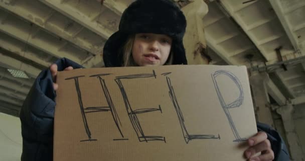 Bottom view of a homeless Syrian girl in dirty clothes standing with Help cardboard and looking at the camera. Hungry frozen refugee living on the streets. — Stock Video