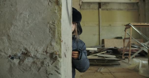 Portret van een Syrische vluchteling in winterkleding verstopt op de bouwplaats met de teddybeer. Bang kind loopt van achter de muur en kijkt naar de camera. — Stockvideo
