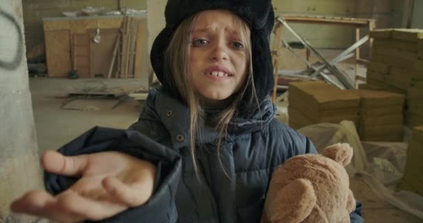 Retrato de um refugiado sírio em roupas sujas de inverno segurando o ursinho de pelúcia e pedindo uma esmola. Menina sem-teto com fome com belos olhos cinzentos recebendo algumas moedas para comida . — Vídeo de Stock