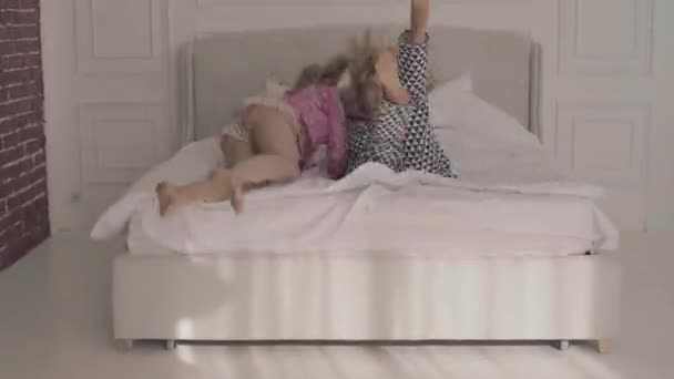 Deux amis caucasiens joyeux sautant sur le lit blanc et riant. Belles filles heureuses ayant pyjama fête à la maison . — Video