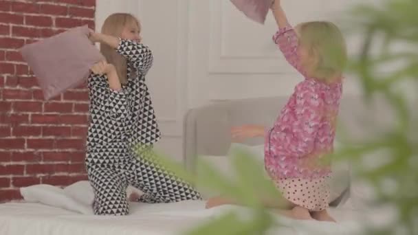 Dois amigos brancos loiros risos lutando com travesseiros na cama branca. Meninas bonitas fazendo festa de pijama no quarto em casa . — Vídeo de Stock