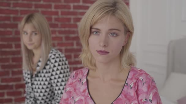 Porträtt av en skadad vit kvinna i rosa pyjamas som sitter med ryggen mot vännen. Blonda vackra flickor grälade med varandra. — Stockvideo
