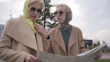 Türbanlı ve güneş gözlüklü iki olgun kadının haritayı tutarak konuşmalarının yakın çekimi. Emeklilikten sonra birlikte seyahat eden son sınıf kadınları..
