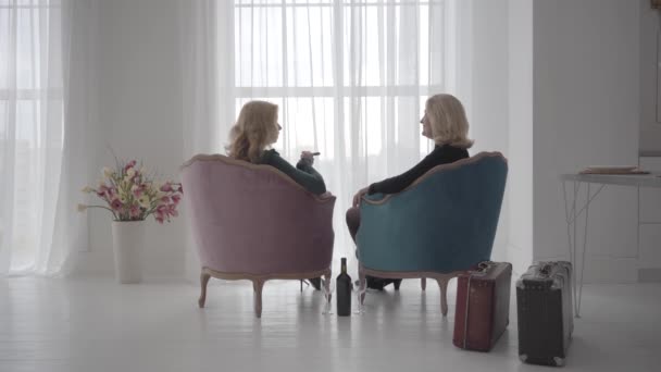 Back view of rich mature Caucasian women sitting in comfortable armchairs and talking. Senior ladies spending vacations with a bottle of wine and cigars. — Stock Video