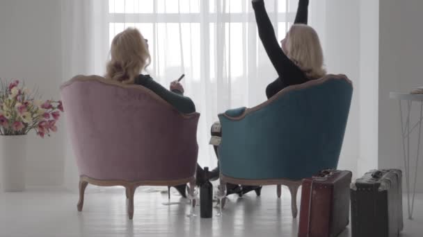Back view of rich Caucasian ladies sitting in comfortable armchairs and throwing money up. Happy wealthy women spending vacations with a bottle of wine and cigars. Slow motion. — Stock Video